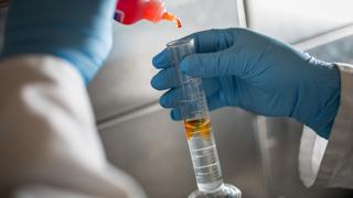 Close up on two gloved hands adding liquid to a measuring beaker